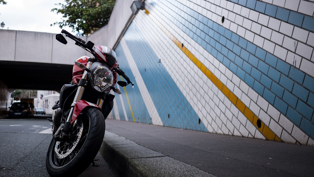 red and black motorcycle parked beside white and blue wall during daytime