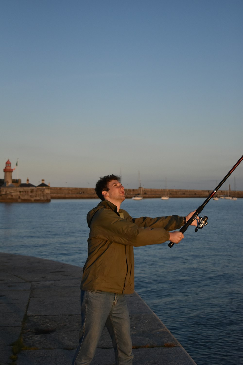 homem em jaqueta marrom segurando vara de pesca em pé na doca durante o dia