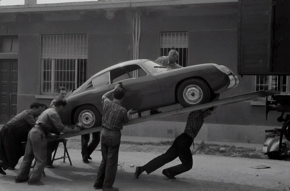 man in black jacket and pants standing beside silver coupe