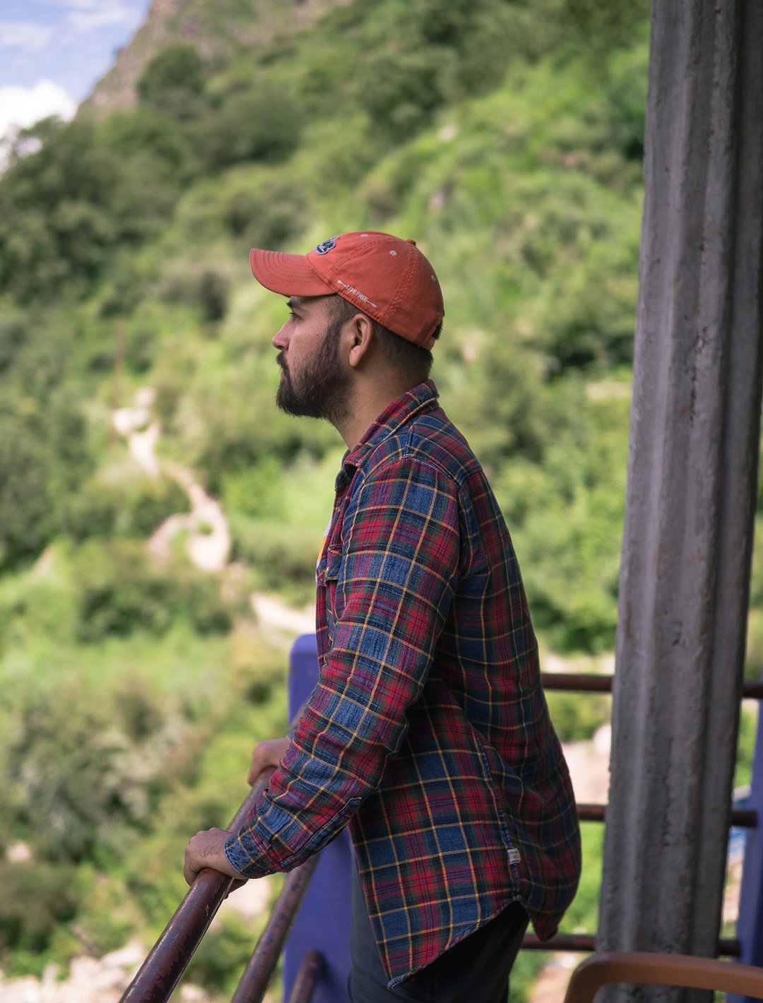 man in blue and red plaid dress shirt wearing orange hat sitting on brown wooden fence