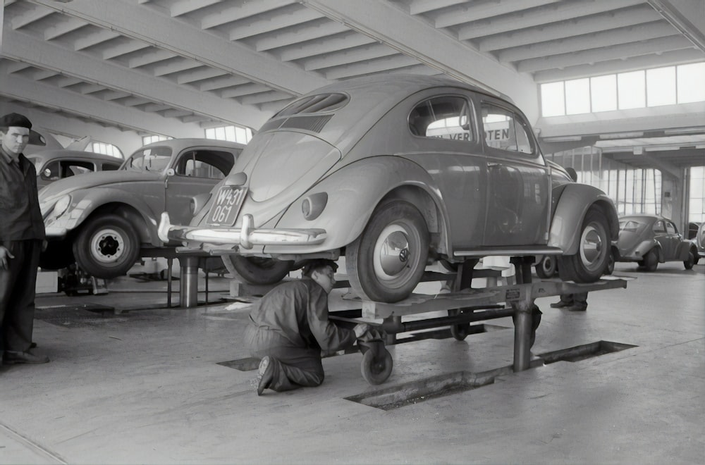 grayscale photo of man in jacket and pants sitting on car