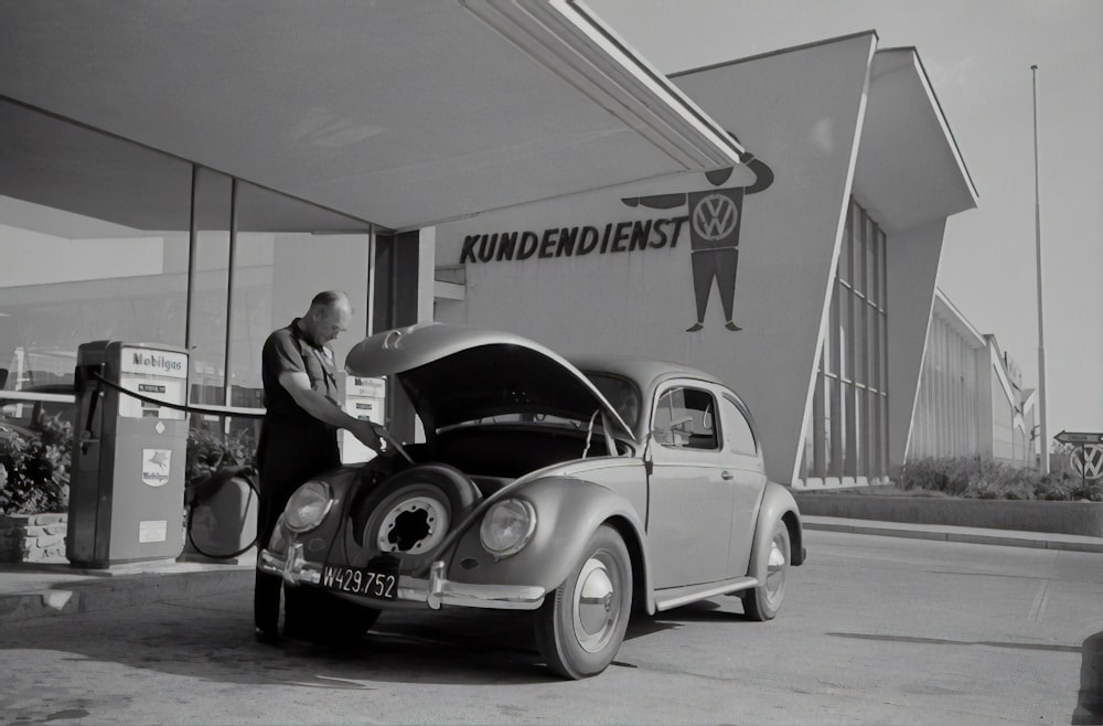 grayscale photo of man and woman standing beside car
