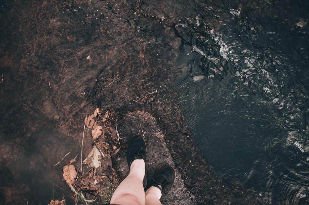 person in black shoes standing on brown rock near body of water during daytime