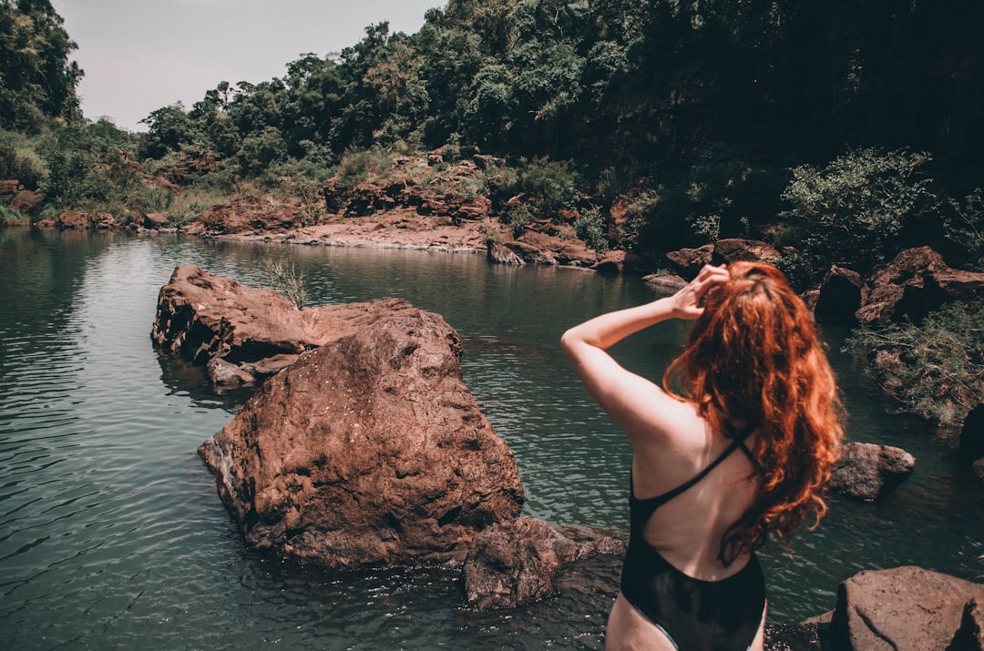 woman in black bikini standing on rock near body of water during daytime
