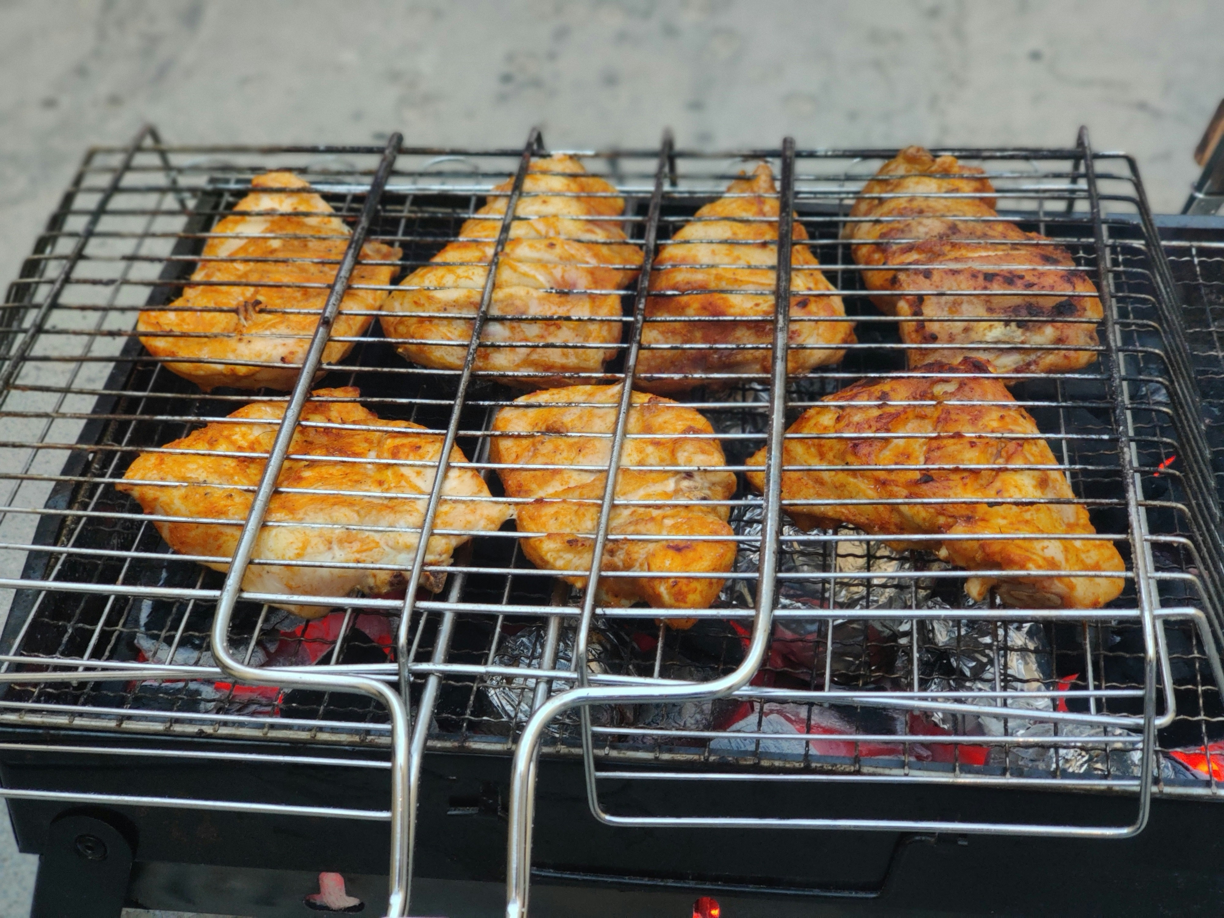 Grilled chicken pieces on charcoal grill, dark grill marks, glowing embers beneath, dim smoky atmosphere
