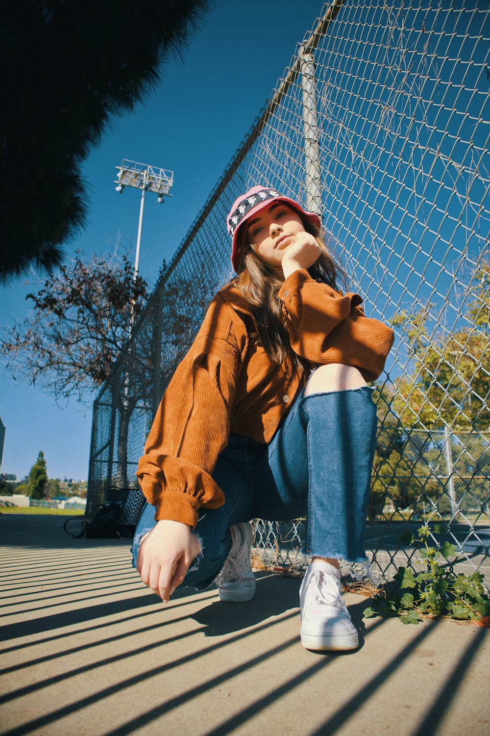 woman in brown coat and blue denim jeans sitting on gray metal fence during daytime