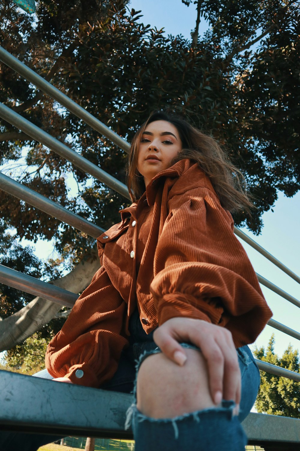 woman in red and blue jacket sitting on gray metal fence during daytime