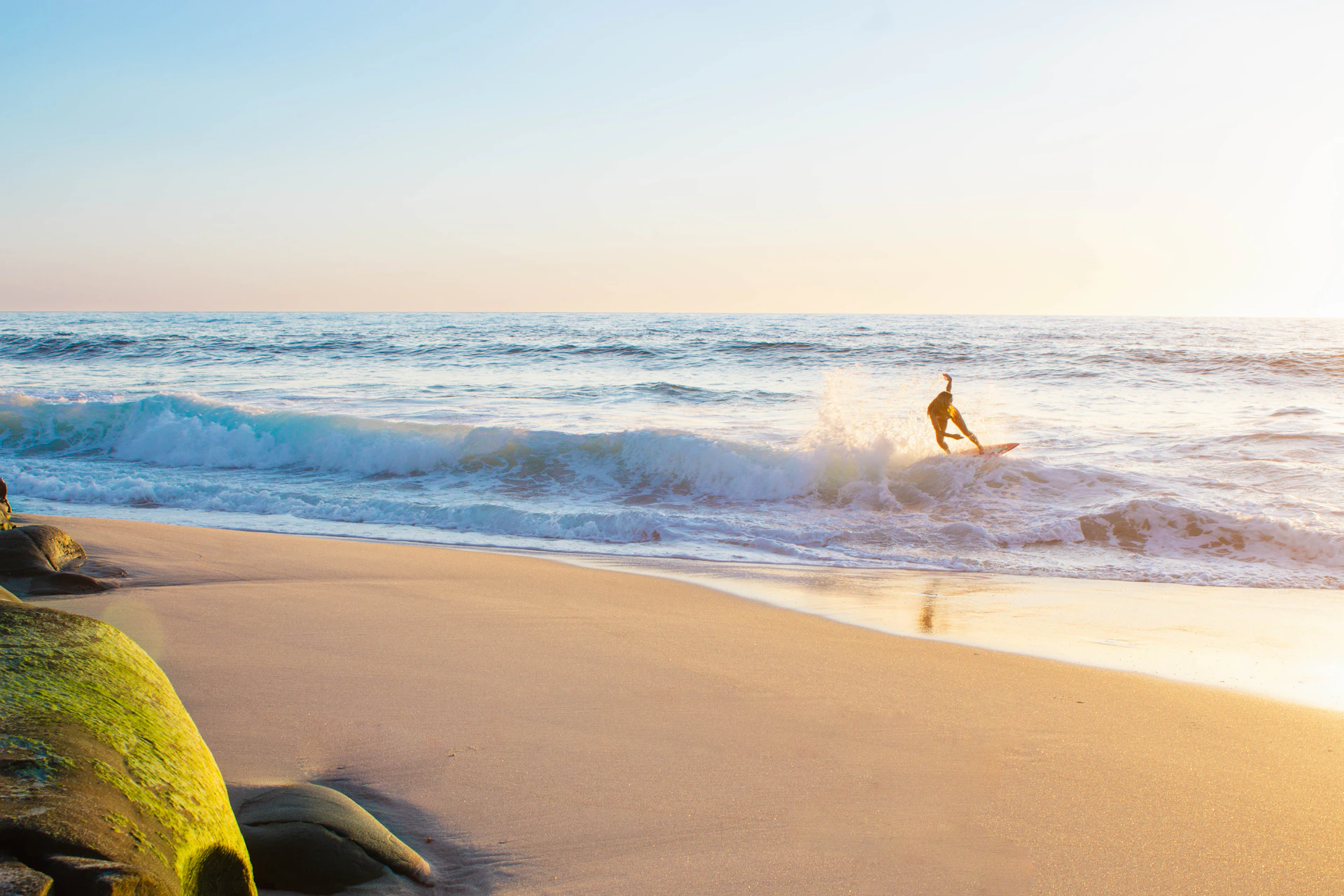 Surfer in wetsuit carrying board, walking toward the water