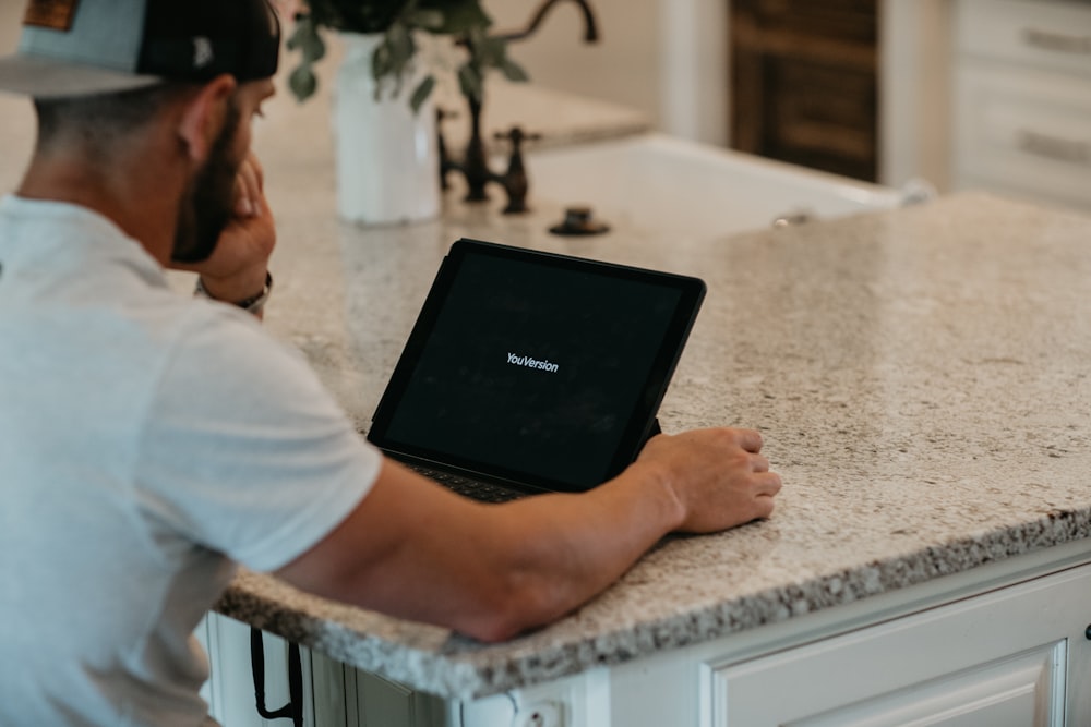 man in white t-shirt using black laptop computer