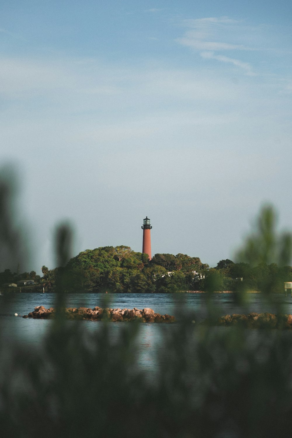 red and white lighthouse on rock formation in the middle of water