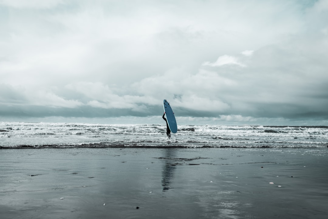 grayscale photo of person holding surfboard on beach