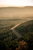 Golden hour light bathes a winding mountain road framed by lush greenery.