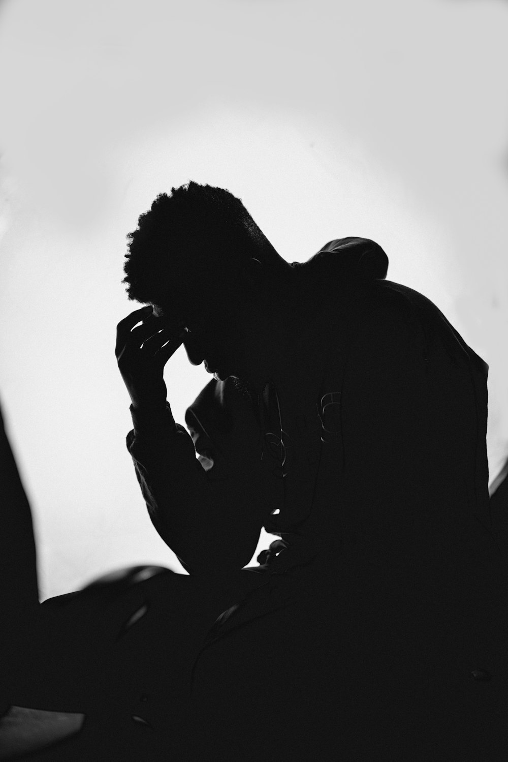 man in black hoodie covering his face with his hands