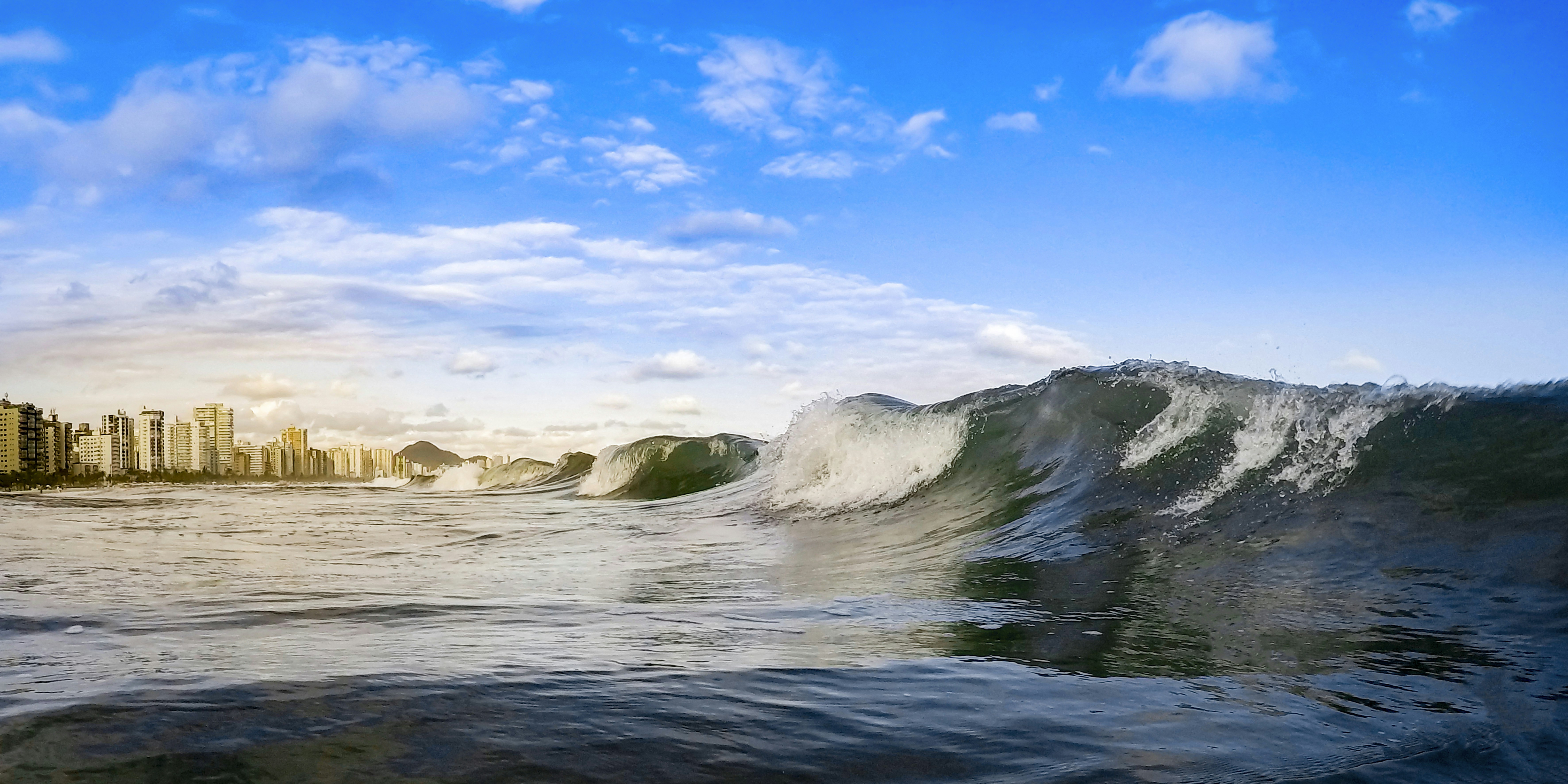 ocean waves crashing on rocks under blue sky and white clouds during daytime