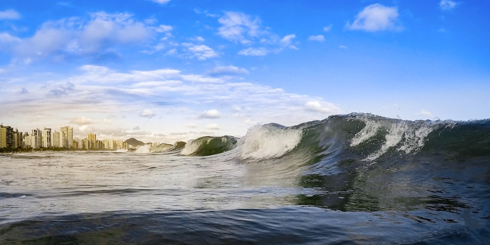 ocean waves crashing on rocks under blue sky and white clouds during daytime