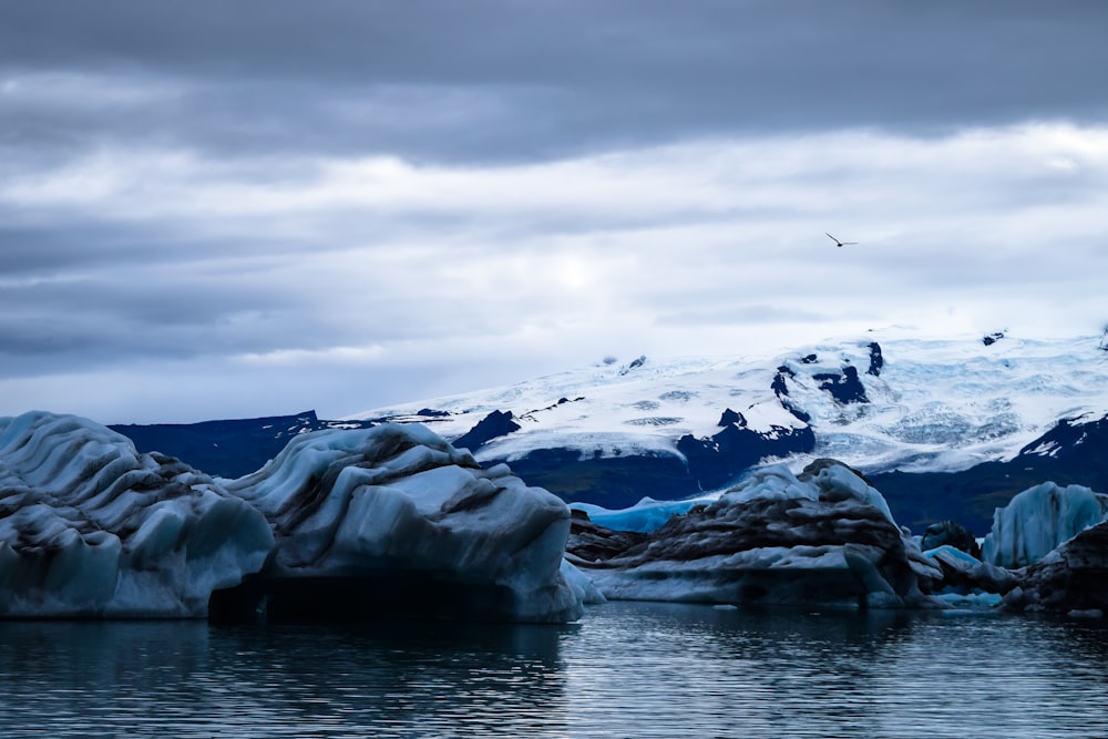 snow covered mountain near body of water under cloudy sky during daytime