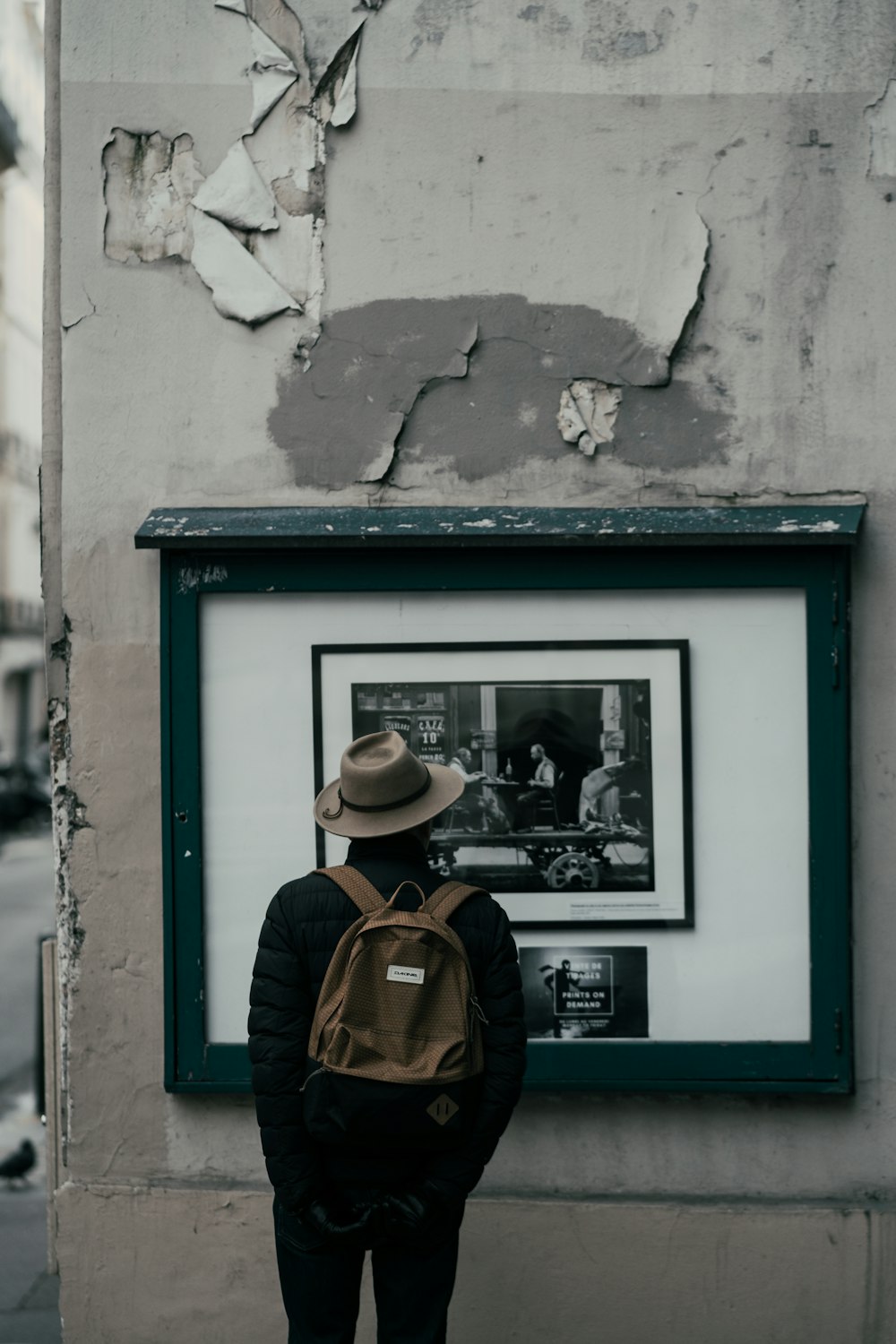 man in brown hat and brown jacket standing in front of blue wooden window