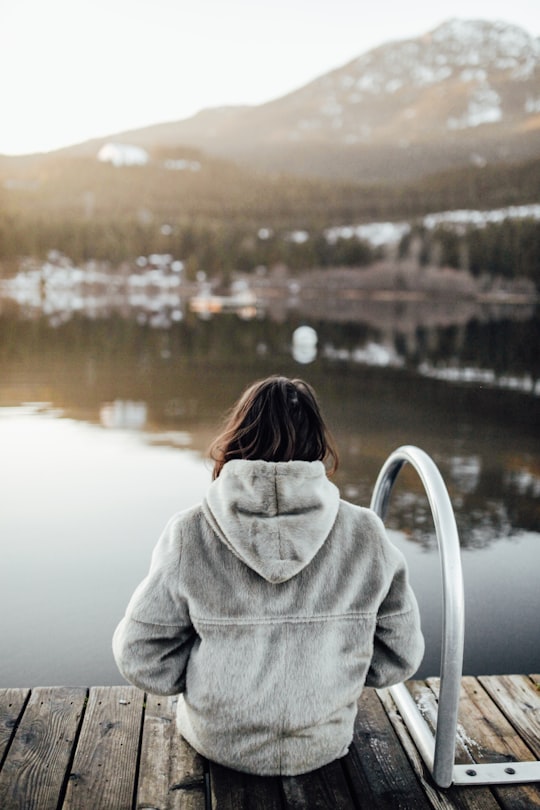 woman in gray hoodie standing near body of water during daytime in Whistler Canada