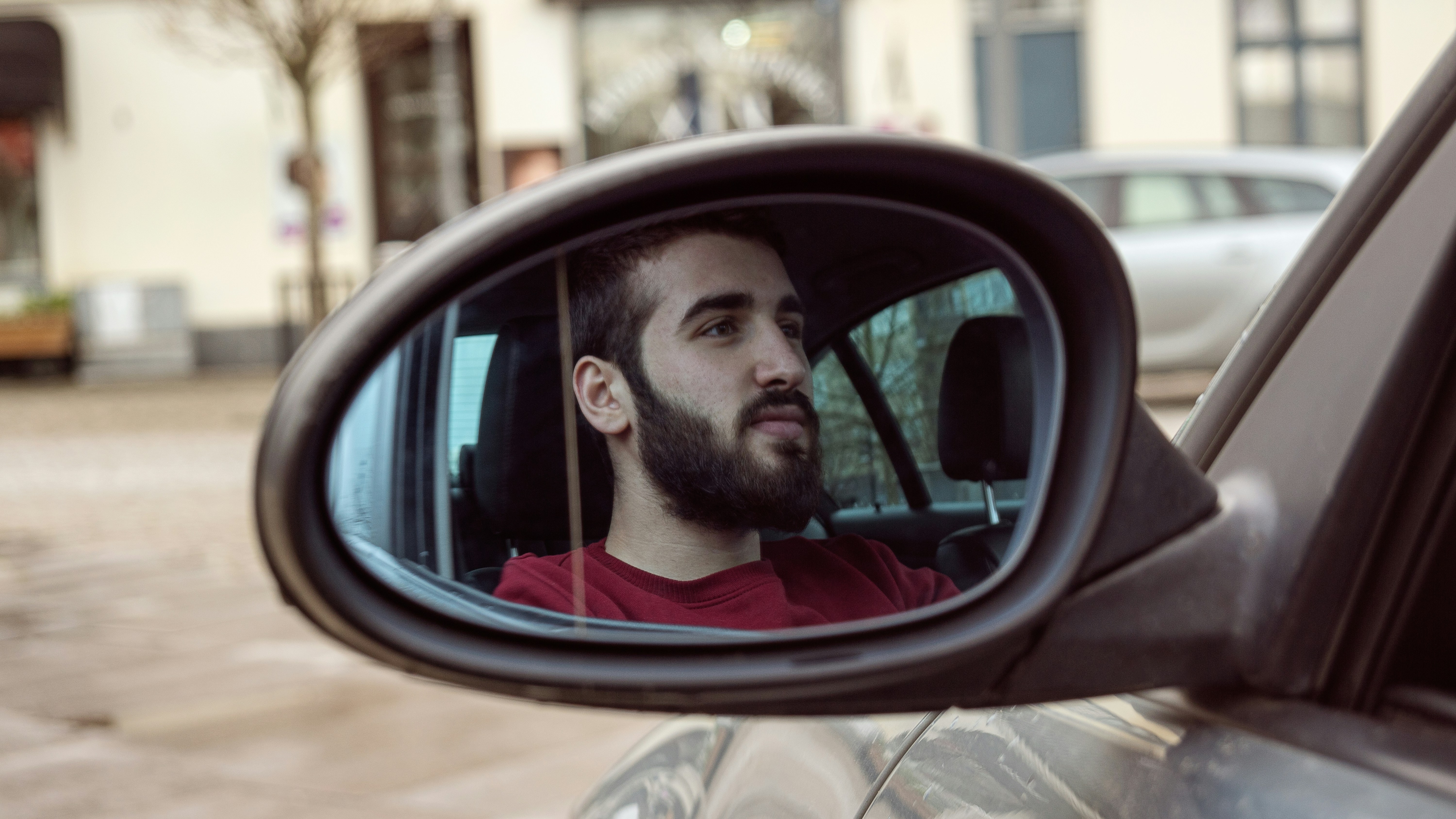 man in red crew neck shirt looking at car side mirror