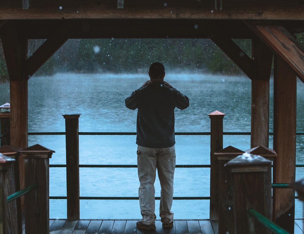 man in black jacket and gray pants standing on brown wooden dock during daytime