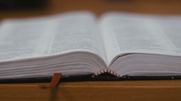 An open book with a deep red bookmark resting on a matte black surface.