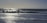 Silhouetted surfers stand with their boards at the edge of the ocean, with waves crashing around them and the sun reflecting off the water's surface.