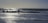Silhouetted surfers stand with their boards at the edge of the ocean, with waves crashing around them and the sun reflecting off the water's surface.