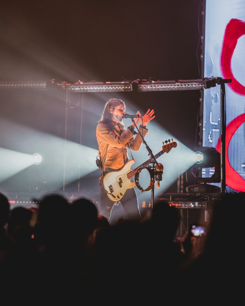 man in brown jacket playing guitar on stage