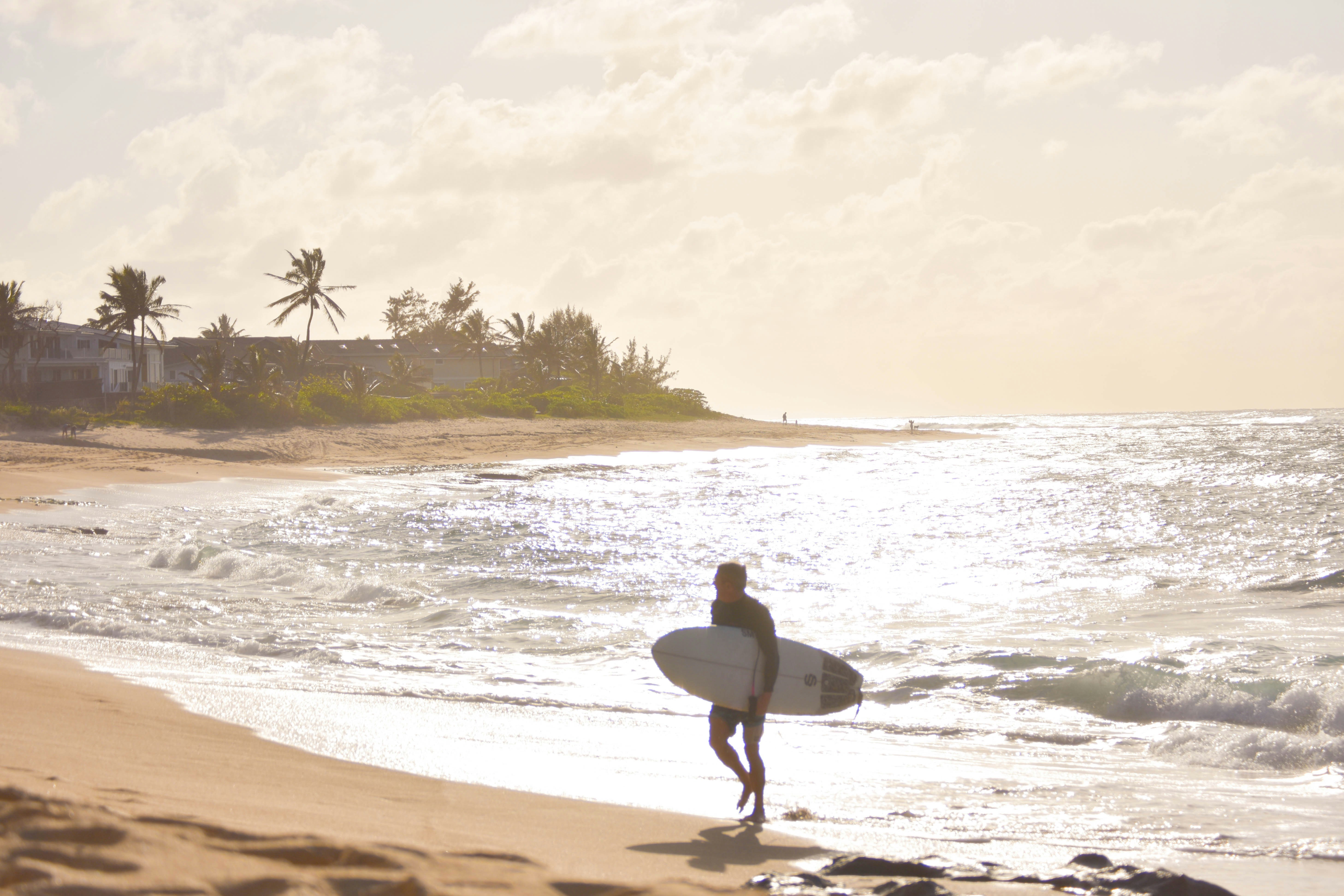 Un homme tenant une planche de surf au sommet d’une plage de sable