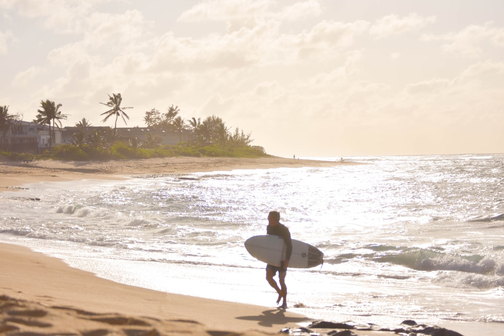 Un homme tenant une planche de surf au sommet d’une plage de sable