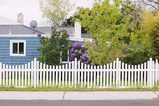 A cozy suburban home bordered by a freshly installed wooden picket fence with vibrant flowers along the base.