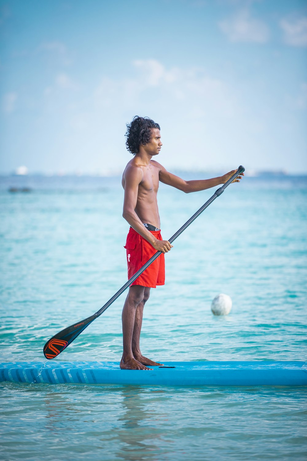 man in red shorts holding red paddle while standing on blue body of water during daytime