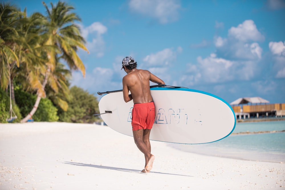 man in red shorts holding white surfboard
