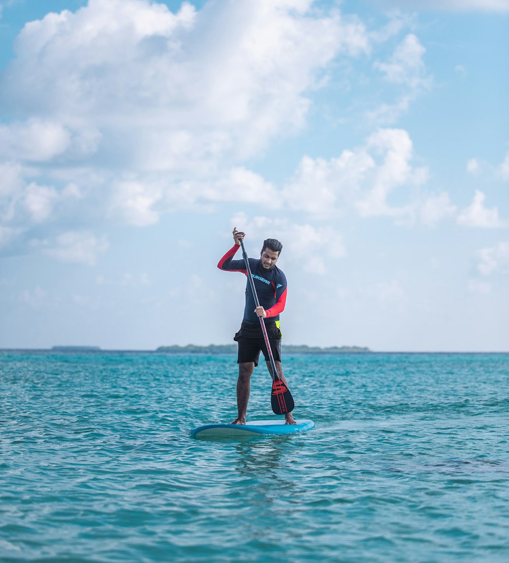 Mann in rotem Hemd und schwarzen Shorts fährt tagsüber auf blauem Surfbrett auf See