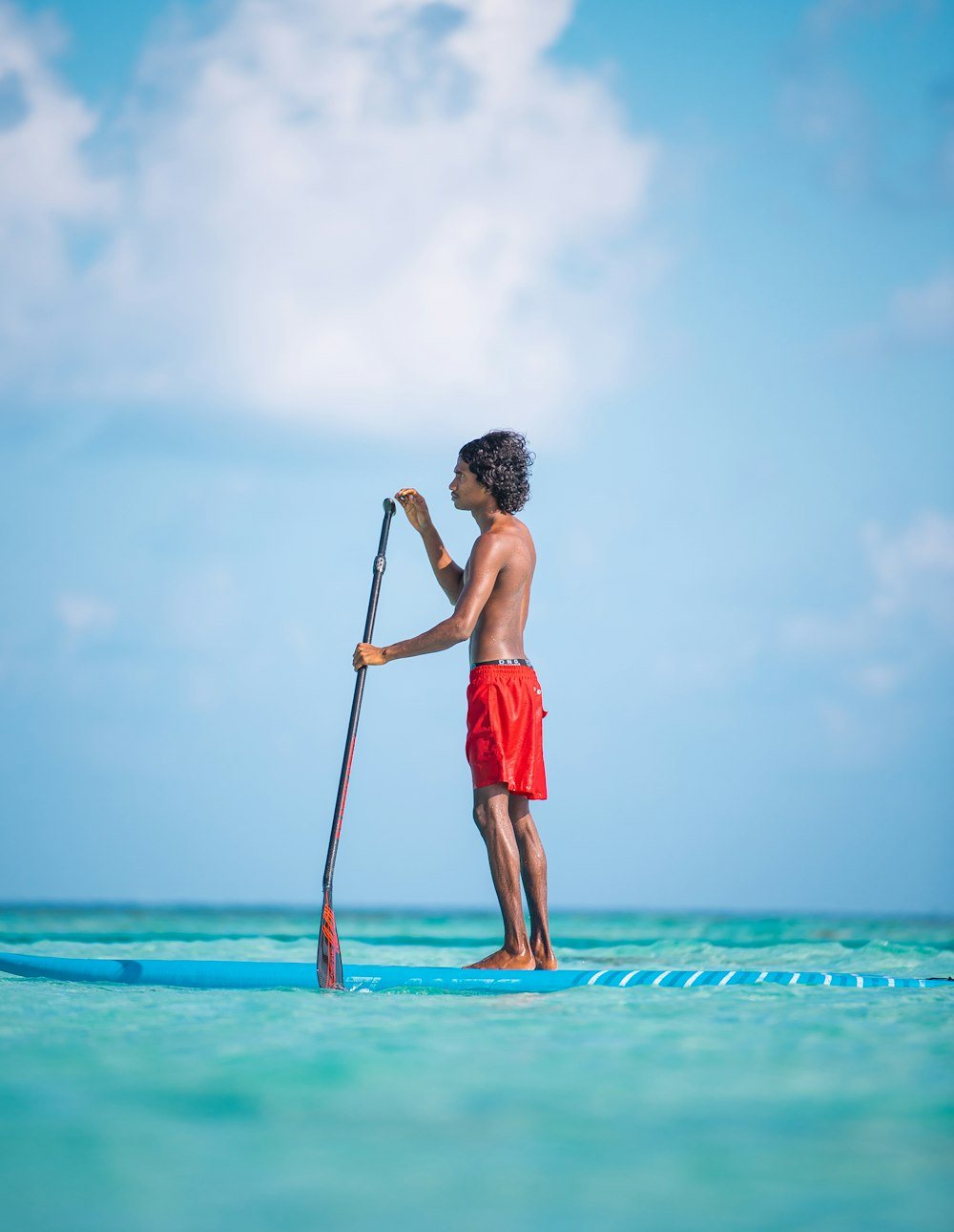 man in red shorts standing on blue sea under white clouds during daytime