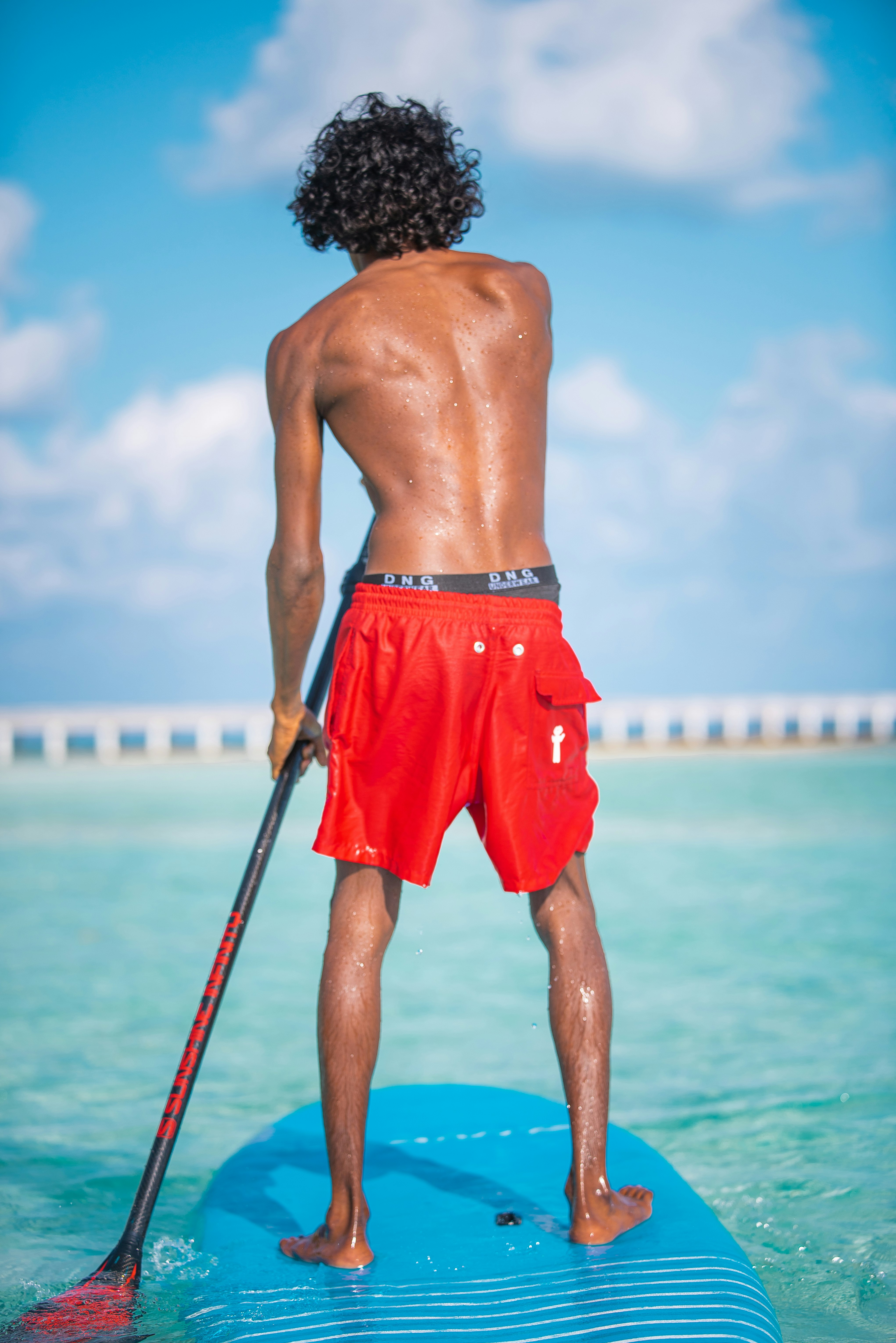 man in red shorts standing on blue and white beach during daytime