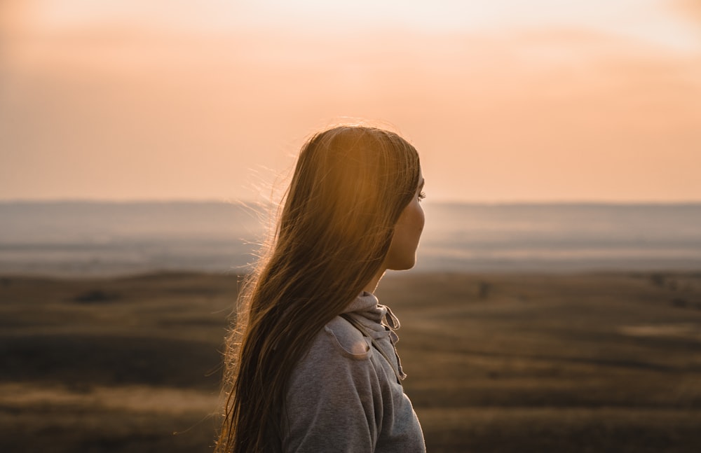 woman in gray hoodie standing on beach during sunset