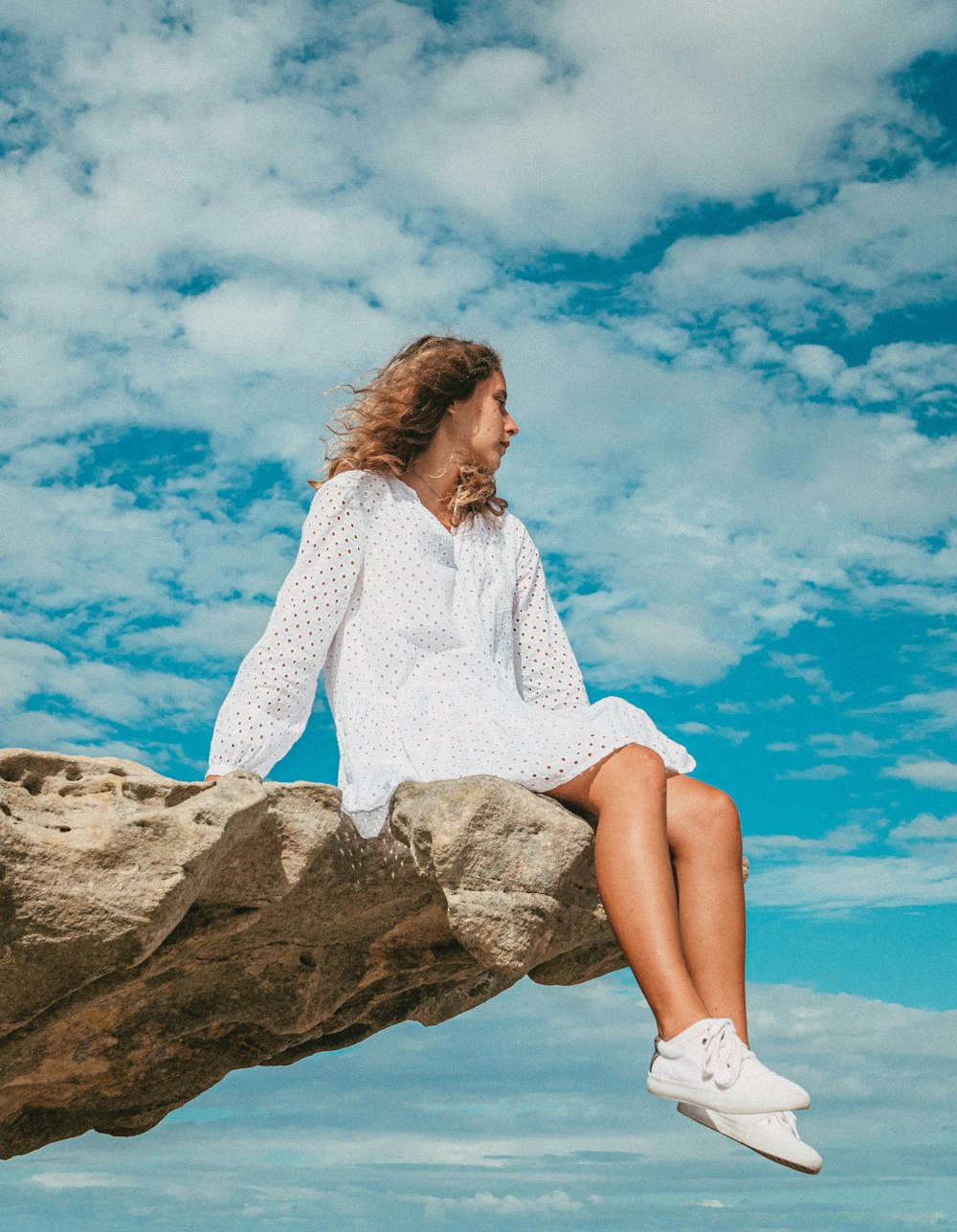 woman in white sweater sitting on brown rock during daytime