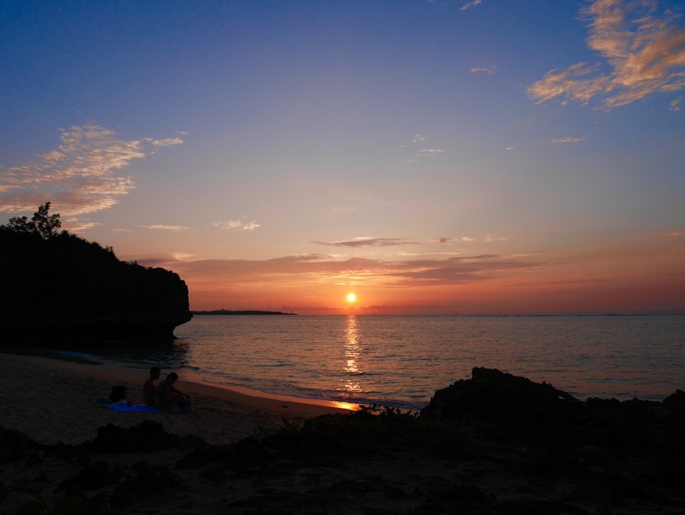 silhouette of person standing on seashore during sunset