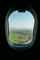 A sleek airplane soaring above a patchwork of green fields and rivers.