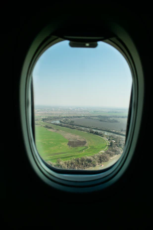 An aerial shot of a plane soaring above a patchwork of green fields and rivers.