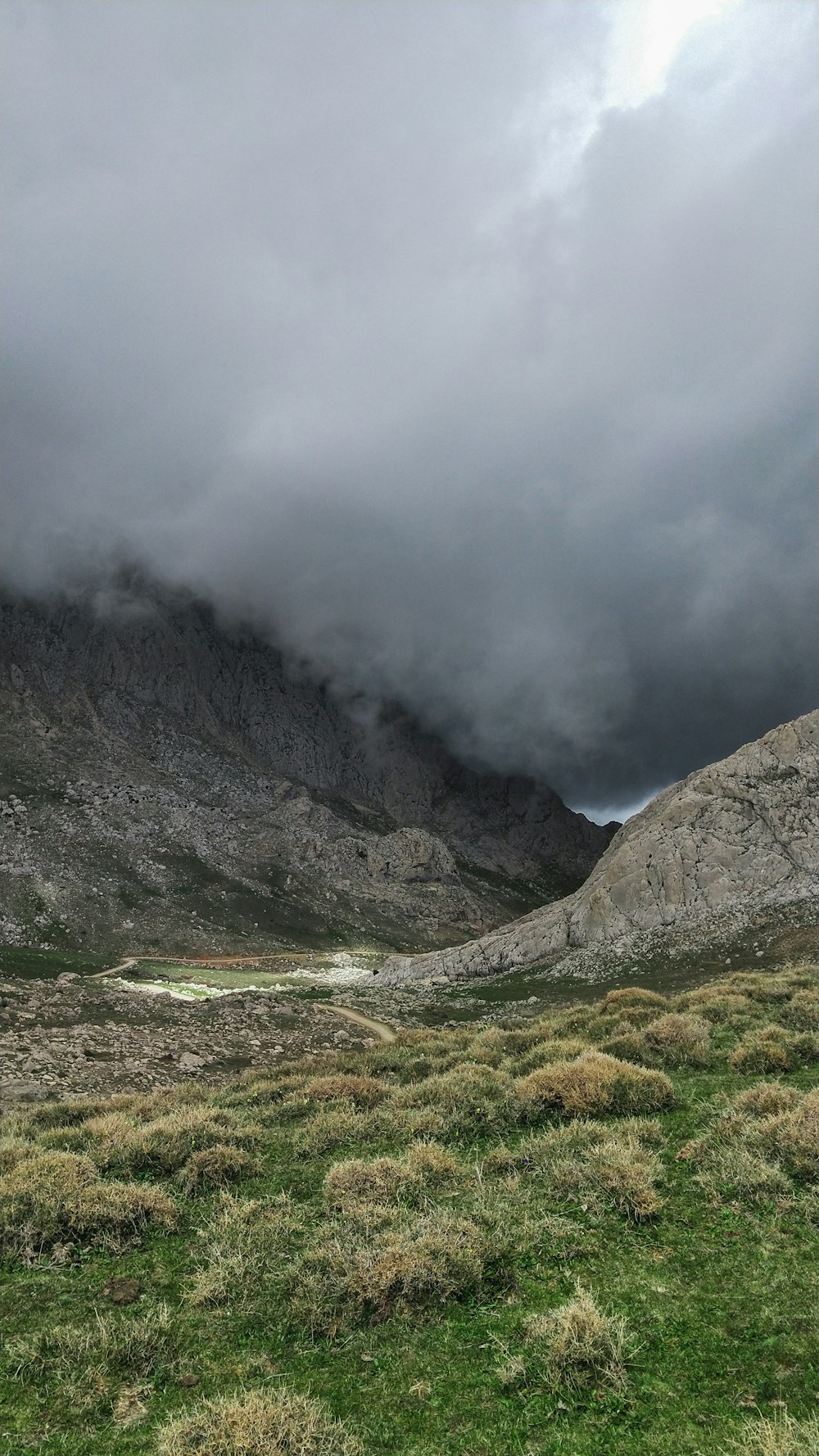 green grass field near mountain under white clouds during daytime