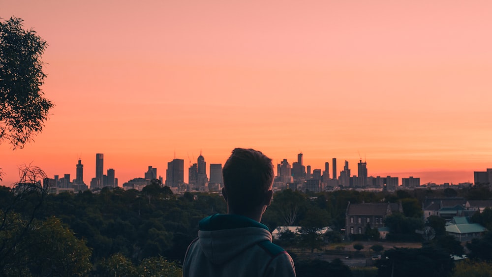 man in green hoodie looking at city buildings during sunset