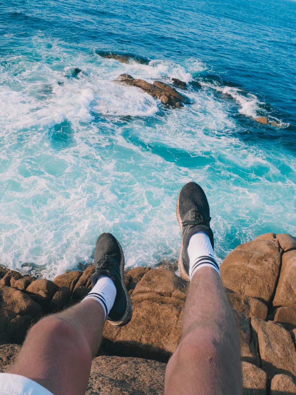 person in brown pants and brown shoes sitting on brown rock near blue sea during daytime