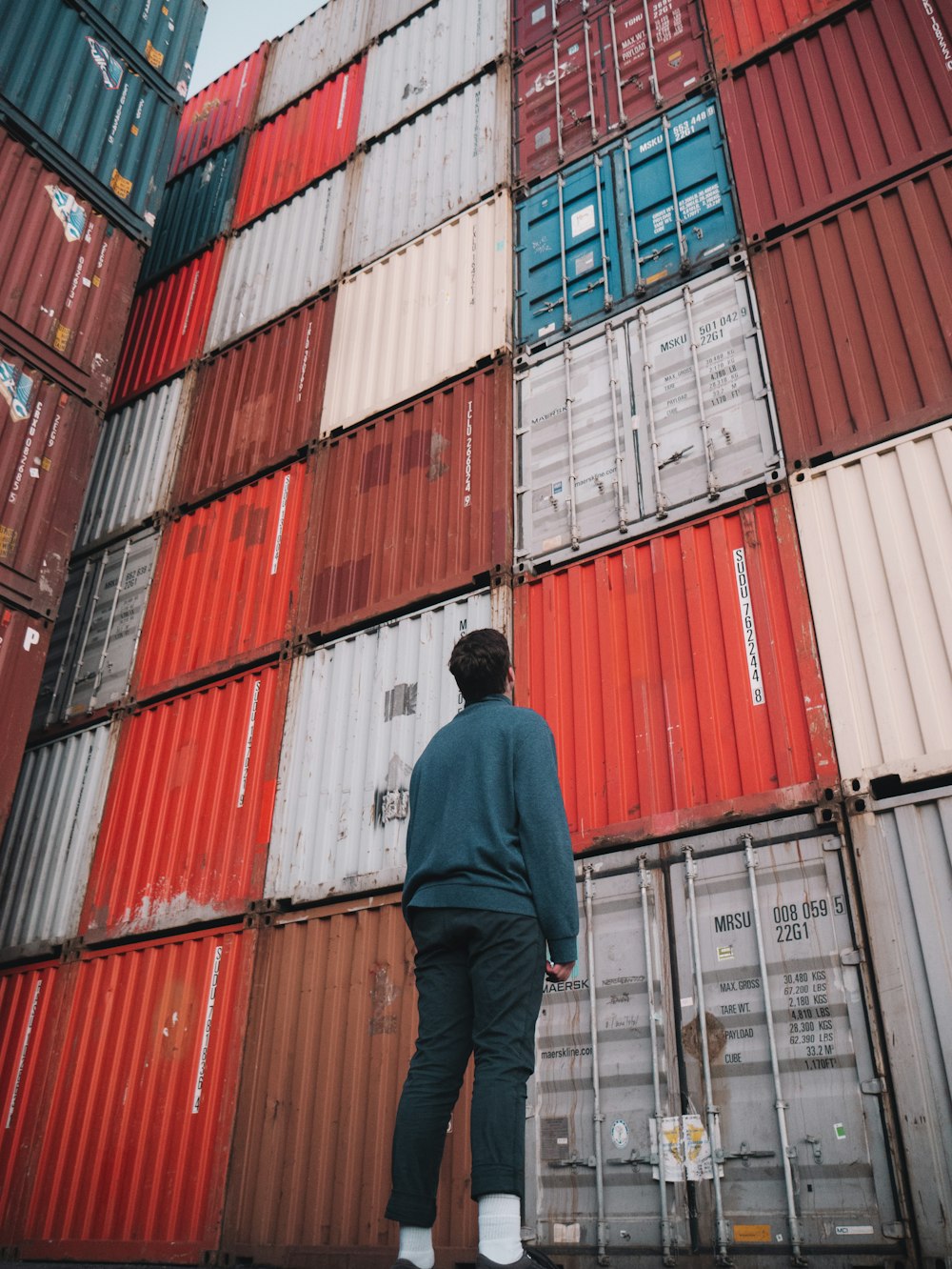 uomo in giacca nera in piedi davanti ai container intermodali rossi e blu