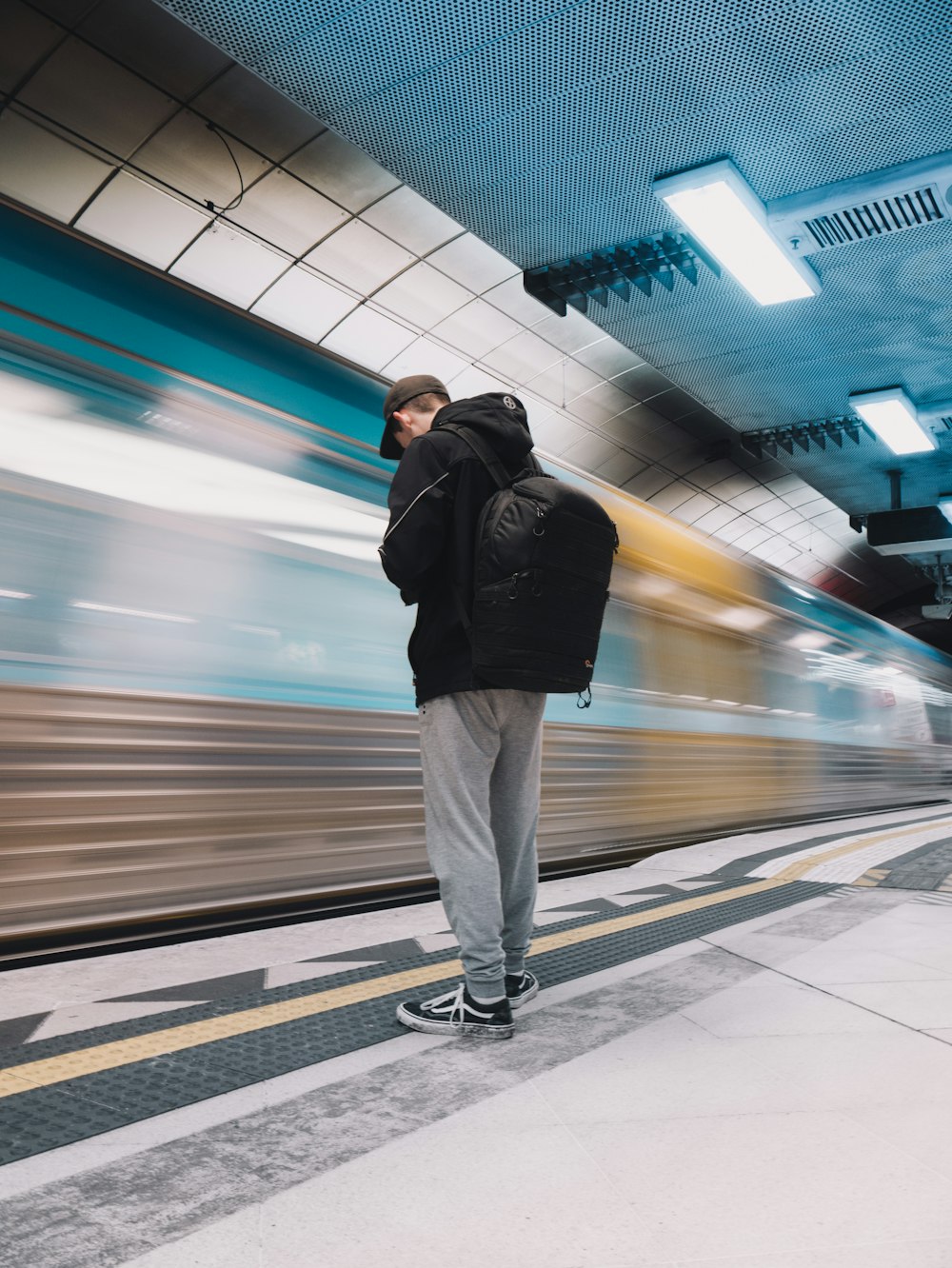 man in black jacket and white pants standing on train station