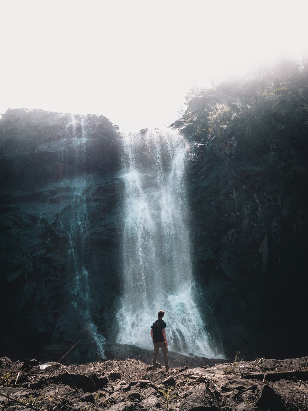 man in black shirt standing on rock near waterfalls during daytime