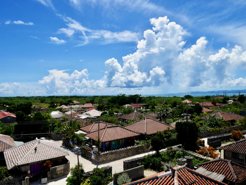 Drone shot capturing whitewashed village rooftops nestled among green hills under a bright blue sky.