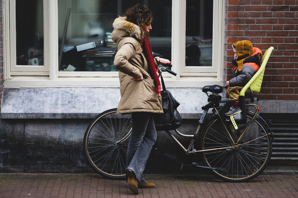 woman in brown coat and blue denim jeans riding on black bicycle