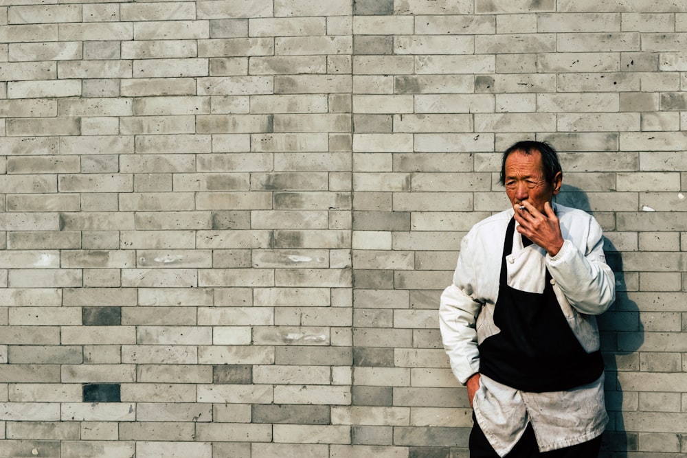man in white dress shirt leaning on gray brick wall